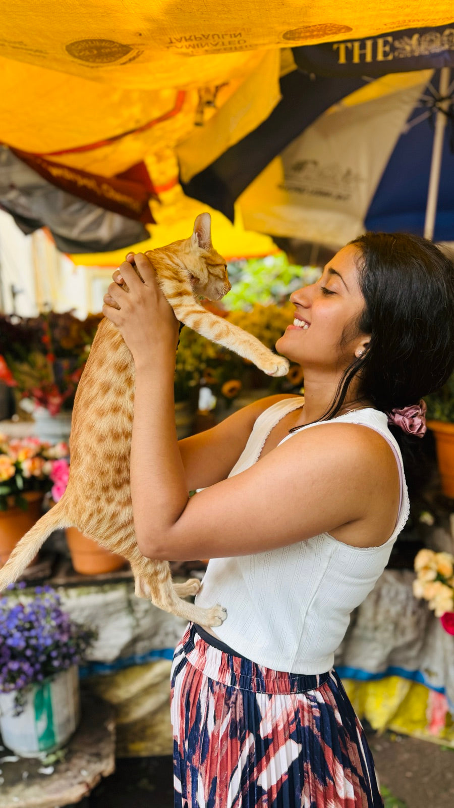 A person joyfully lifting a rescued ginger cat face-to-face at a flower market
