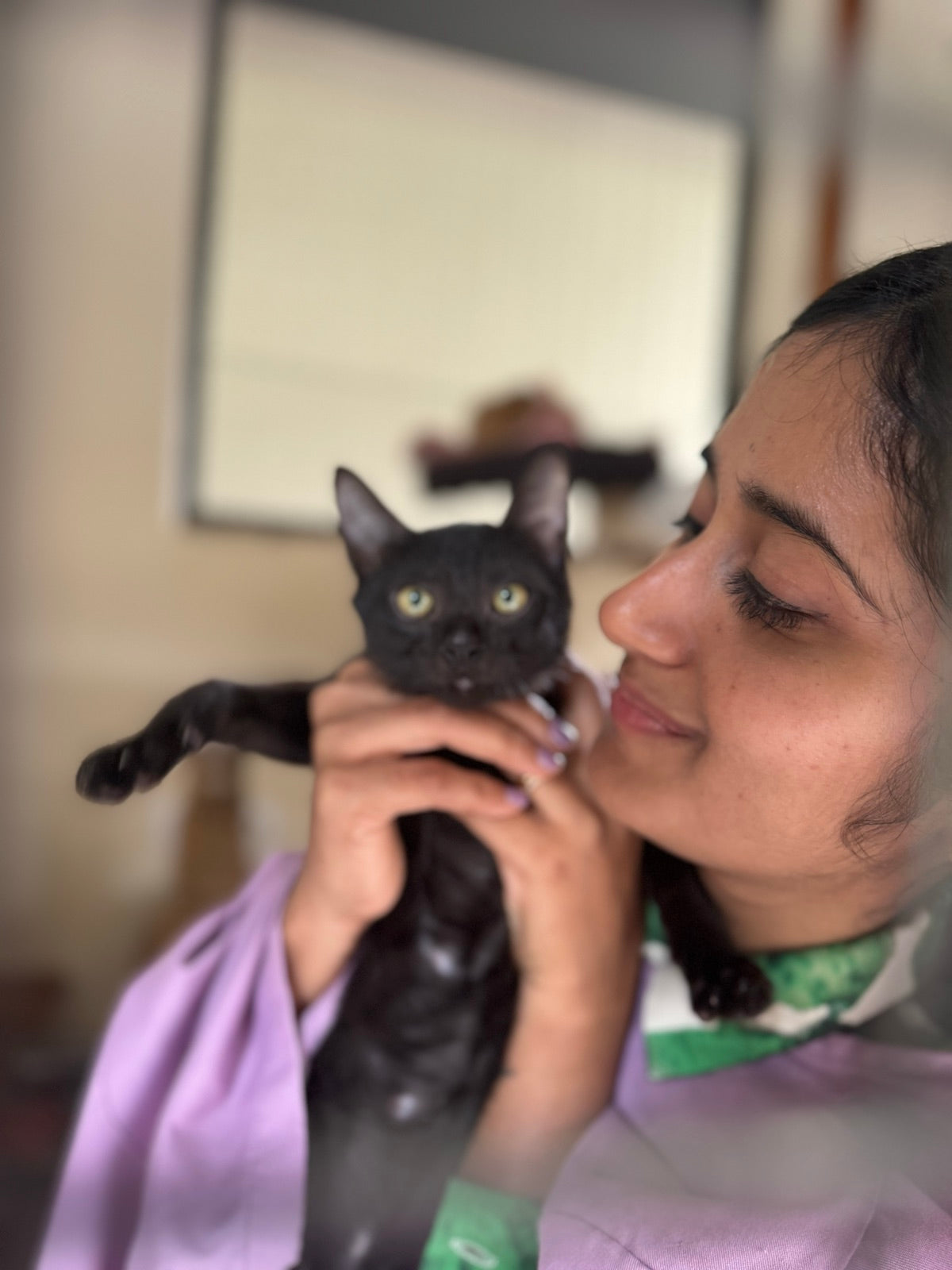 A person cradling a rescued black kitten close to their cheek